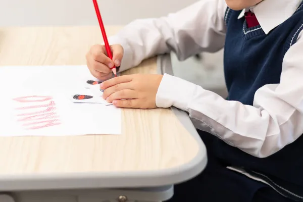 1年生の少年は 白いテーブルに座っている間 白い紙の上に赤い明るい鉛筆でハロウィンの休日のためのポストカードを描きます 選択的フォーカス ぼっけ — ストック写真