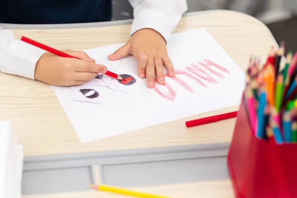 一年级男孩坐在白桌旁 用一支红色明亮的铅笔在白纸上画了一张明信片来庆祝光晕假期 有选择的重点 Bokeh — 图库照片