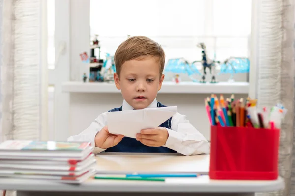 一个在家里穿着校服的一年级可爱男孩在课间休息时独自坐在办公桌前 制造了一架纸飞机 有选择的重点 肖像画 — 图库照片