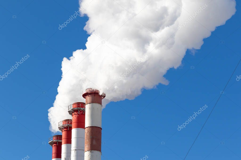 red-white chimneys of the boiler room, equipped with a traffic light. white smoke against blue sky on sunny frosty winter day