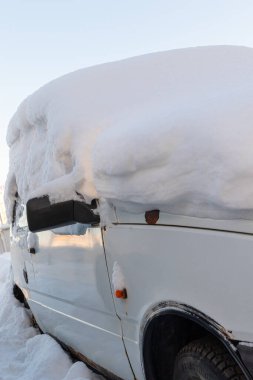 Eski beyaz terk edilmiş paslı araba soğuk bir kış gününde yol kenarında büyük bir kar tabakasının altına park edilmiş.