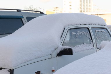 Eski beyaz terk edilmiş paslı araba soğuk bir kış gününde yol kenarında büyük bir kar tabakasının altına park edilmiş.