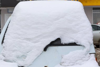 Eski beyaz terk edilmiş paslı araba soğuk bir kış gününde yol kenarında büyük bir kar tabakasının altına park edilmiş.