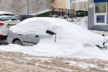 Soğuk bir kış gününde yolun kenarında, büyük bir kar tabakasının altına park edilmiş eski terk edilmiş bir araba.