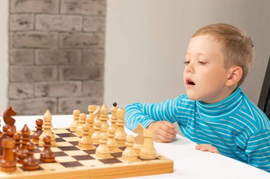 Evde beyaz tahta bir masada satranç oynayan yedi yaşında tatlı bir çocuk. Seçici odaklanma. Yakın plan. Portre