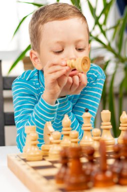 Evde beyaz tahta bir masada satranç oynayan yedi yaşında tatlı bir çocuk. Seçici odaklanma. Yakın plan. Portre
