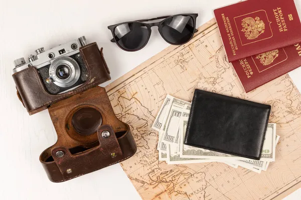 世界地图 两张护照 一个黑色皮夹里的钱 一个皮箱里的旧胶卷相机和一个白色木制桌子上的太阳镜 从上面看 有选择的重点 护照俄罗斯联邦 — 图库照片