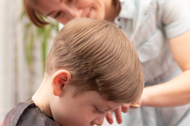 Genç anne kuaför karantina sırasında bebeğini saç makasıyla keser. Seçici odaklanma. portre