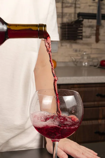 女性の手はキッチンの黒い木のテーブルの上に瓶から赤ワインをグラスに注ぐ 選択的焦点 — ストック写真