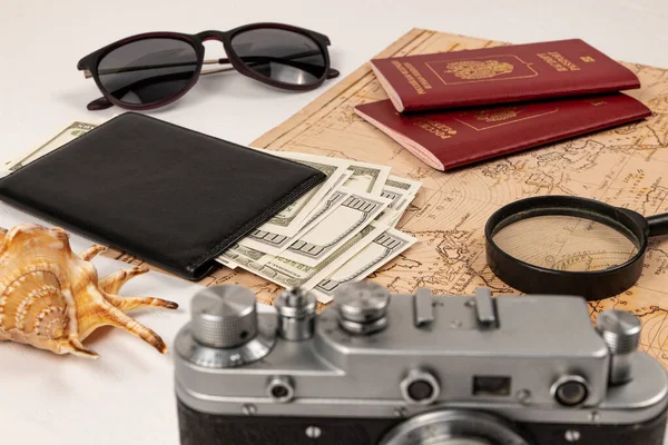 世界地图 两张护照 一个放大镜 一个黑皮钱包里的钱 一个旧胶卷相机 太阳镜和一个白色木制桌子上的外壳 有选择的重点 护照俄罗斯联邦 — 图库照片