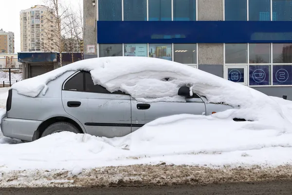 Soğuk bir kış gününde yolun kenarında, büyük bir kar tabakasının altına park edilmiş eski terk edilmiş bir araba.