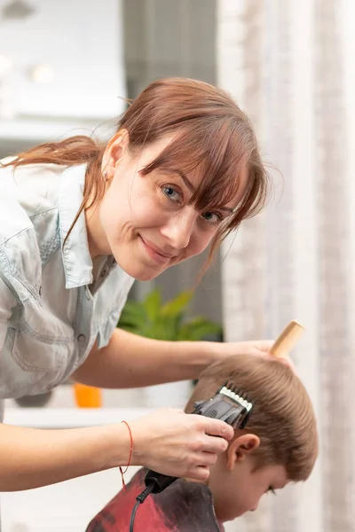 在检疫期间 年轻的妈妈理发师在家里用剪子剪她的男婴 有选择的重点 肖像画 免版税图库照片