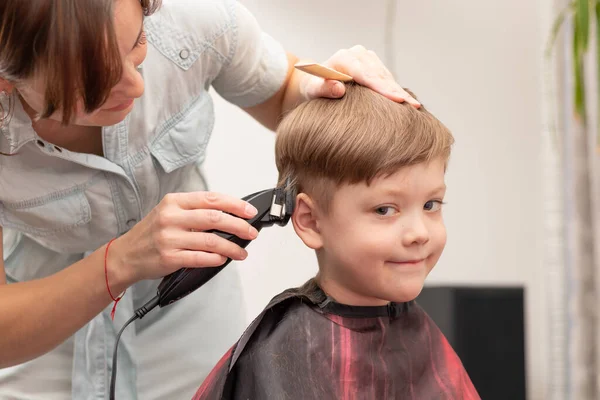 在检疫期间 年轻的妈妈理发师在家里用剪子剪她的男婴 有选择的重点 肖像画 图库图片