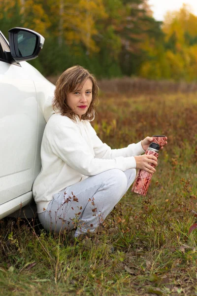 Ładna Młoda Kobieta Białej Bluzie Siedzi Pobliżu Białego Samochodu Termosem — Zdjęcie stockowe