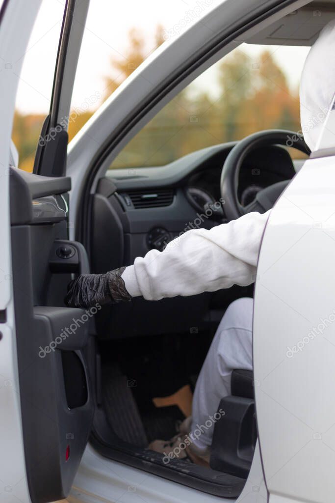 A man in a white sweater with a hood sits at the wheel of a car and tries to start it in order to steal it. Selective focus. Close-up