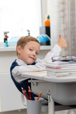 Okulun birinci sınıf üniformalı tatlı bir çocuk, mola sırasında masasında otururken aylaklık ediyor. Seçici odaklanma. Yakın plan. Portre