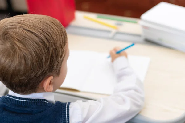一个穿着校服的可爱的一年级男孩坐在办公桌前 手里拿着铅笔 一边做作业 远程教育 有选择的重点 肖像画 — 图库照片