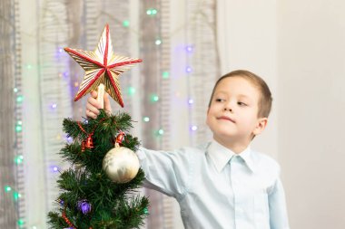 Yedi yaşında gömlekli bir çocuk Noel ağacını Noel arifesinde evde çelenklerle süslüyor. Seçici odaklanma. Portre