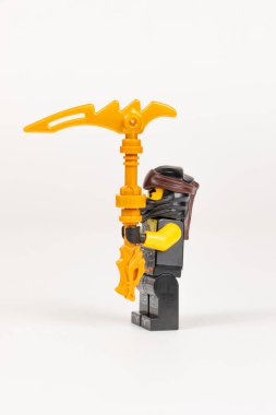 Yekaterinburg 'da. - Rusya. 04.08.2021. Siyah kimonolu oyuncak kahraman Cole 'un beyaz bir arka planda lego ninjalarından çıkan altın bir silah depremi tırpanı var. Yakın plan. seçici odak