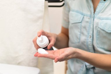 Mavi bornozlu genç bir kadın banyodaki eline makyaj çıkarıcı sürüyor. Seçici odaklanma. Yakın plan.