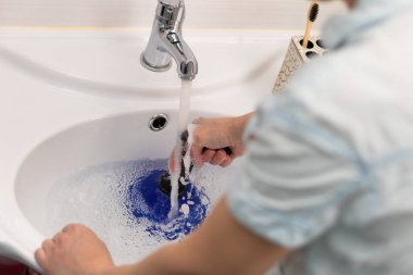 Parlak bir banyodaki kadın temizleyici lavabodaki tıkanıklığı pompayla temizliyor. Seçici odaklanma. Yakın plan.