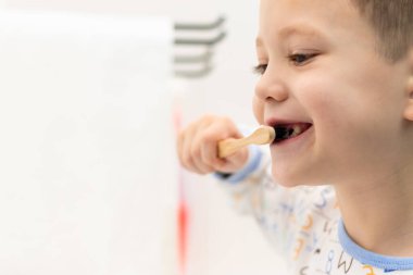 Elinde bambu diş fırçası olan yedi yaşında tatlı bir çocuk banyoda yatmadan önce dişlerini fırçalar. Seçici odaklanma. Portre