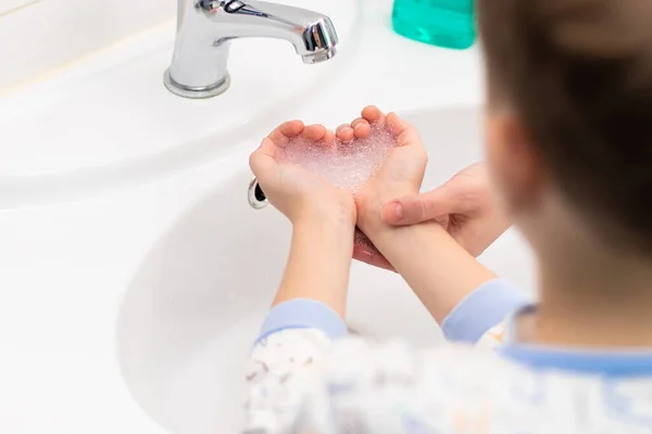 洗面台の上に子供の手の中の心の形で石鹸泡と明るいバスルームで母親の手 選択的フォーカス — ストック写真