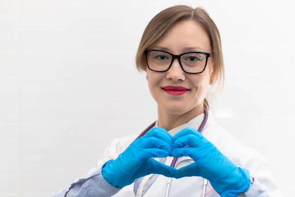 Tıp eldivenleri ve gözlüklü, hastanede steteskobu olan genç ve güzel doktor kadın el hareketlerini gösteriyor. Seçici odaklanma. Portre. Yakın plan.