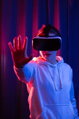 Sanal gerçeklik gözlüklü genç bir kadın ve mavi menekşe arka planda beyaz kapüşonlu bir kazak. Modern teknolojiler. Seçici odaklanma. Portre