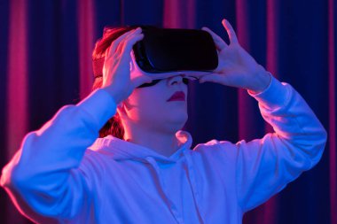 Sanal gerçeklik gözlüklü genç bir kadın ve mavi menekşe arka planda beyaz kapüşonlu bir kazak. Modern teknolojiler. Seçici odaklanma. Portre