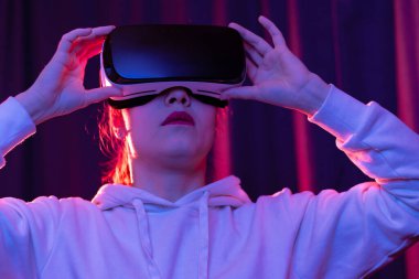 Sanal gerçeklik gözlüklü genç bir kadın ve mavi menekşe arka planda beyaz kapüşonlu bir kazak. Modern teknolojiler. Seçici odaklanma. Portre