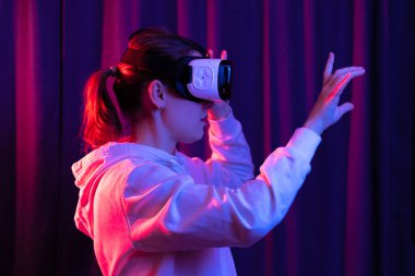 Sanal gerçeklik gözlüklü genç bir kadın ve mavi menekşe arka planda beyaz kapüşonlu bir kazak. Modern teknolojiler. Seçici odaklanma. Portre