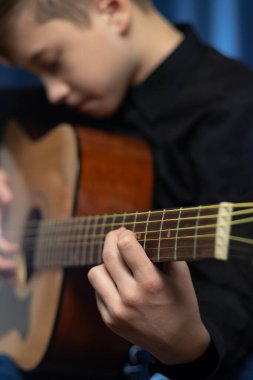 Siyah gömlekli genç bir adam mavi arka planda bir konserde akustik gitar çalar. Hobi olarak. Müzik aletleri. Seçici odaklanma. Portre