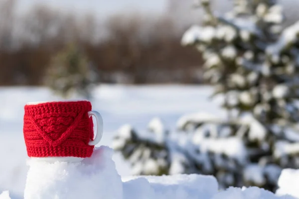 雪に覆われたモミの木を背景に森の中の霜の晴れた冬の日に雪のドリフトで熱い飲み物を持つ赤いマグカップ 選択的フォーカス — ストック写真