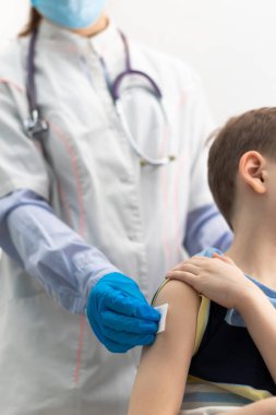 Beyaz önlüklü bir doktor ve fonendoskoplu lastik eldivenli bir doktor salgın sırasında bir çocuk için koronavirüs aşısı yapar. Seçici odaklanma. Portre