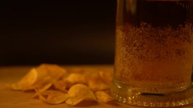 Bardakta bira ve cips, tahtada siyah zemin üzerinde.