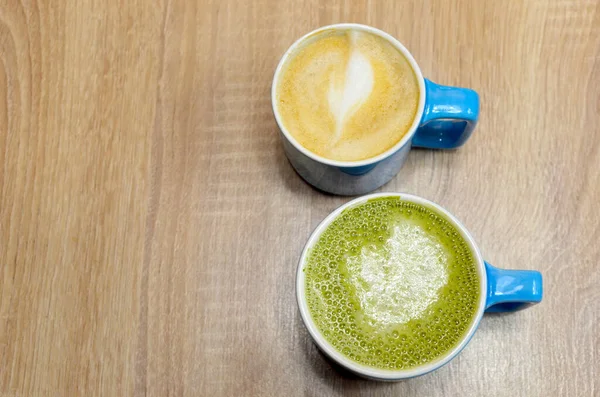 Two blue mugs with cappuccino and matcha teaon a wooden table — Foto de Stock