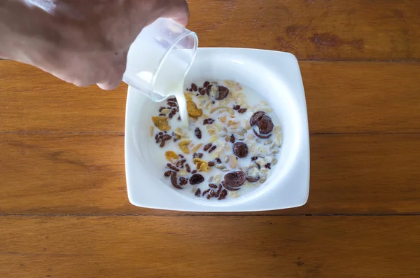 Coloque o leite em disco com muitos flocos de milho na mesa de madeira — Fotografia de Stock