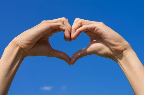 Handen vormen zijn hart voor de liefde met blauwe hemel — Stockfoto
