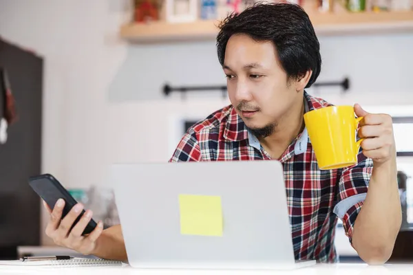 Evde Çalışan Asyalı Bir Adam Mutfak Odasında Bilgisayar Cep Telefonuyla — Stok fotoğraf