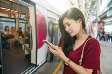 Asyalı kadın yolcu seyahat büyük şehir, yaşam tarzı ve ulaşım kavramında Bts Skytrain raylar veya Mrt metro akıllı cep telefonu kullanarak rahat takım elbise ile