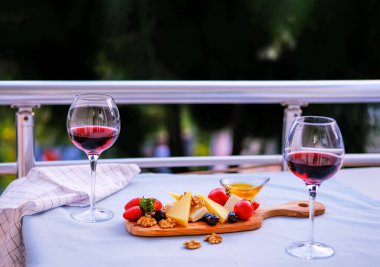 Balkondaki masada iki bardak kırmızı şarap ve peynir tabağı. Evde güzel yemekler..
