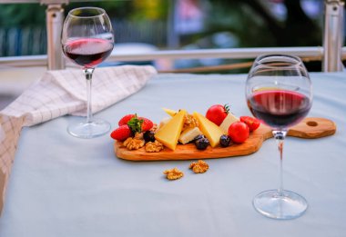 Balkondaki masada iki bardak kırmızı şarap ve peynir tabağı. Evde güzel yemekler..