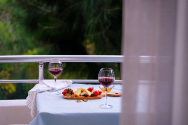 Balkondaki masada iki bardak kırmızı şarap ve peynir tabağı. Evde güzel yemekler..