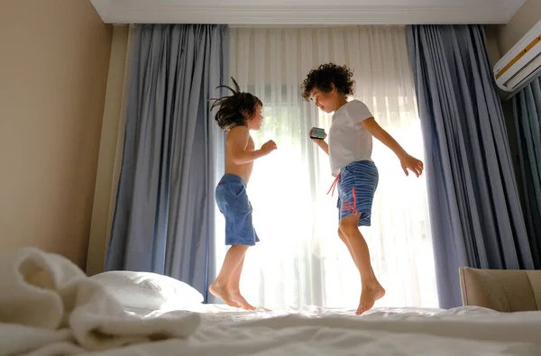 Deux enfants heureux sautant sur le lit avec un téléphone écoutant de la musique Image En Vente