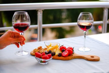 Balkondaki masada iki bardak kırmızı şarap ve peynir tabağı. Evde güzel yemekler..