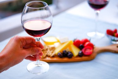 Balkondaki masada iki bardak kırmızı şarap ve peynir tabağı. Evde güzel yemekler..