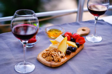 Balkondaki masada iki bardak kırmızı şarap ve peynir tabağı. Evde güzel yemekler..