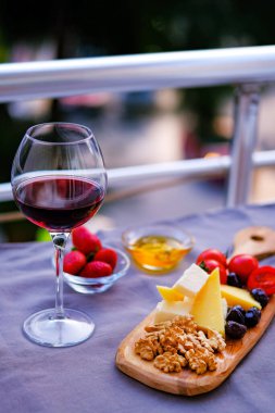 Balkondaki masada iki bardak kırmızı şarap ve peynir tabağı. Evde güzel yemekler..