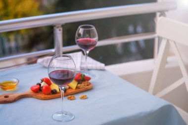Balkondaki masada iki bardak kırmızı şarap ve peynir tabağı. Evde güzel yemekler..